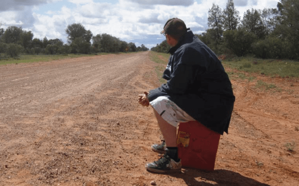 A service crew member sitting on a jerry can waiting for their car. 